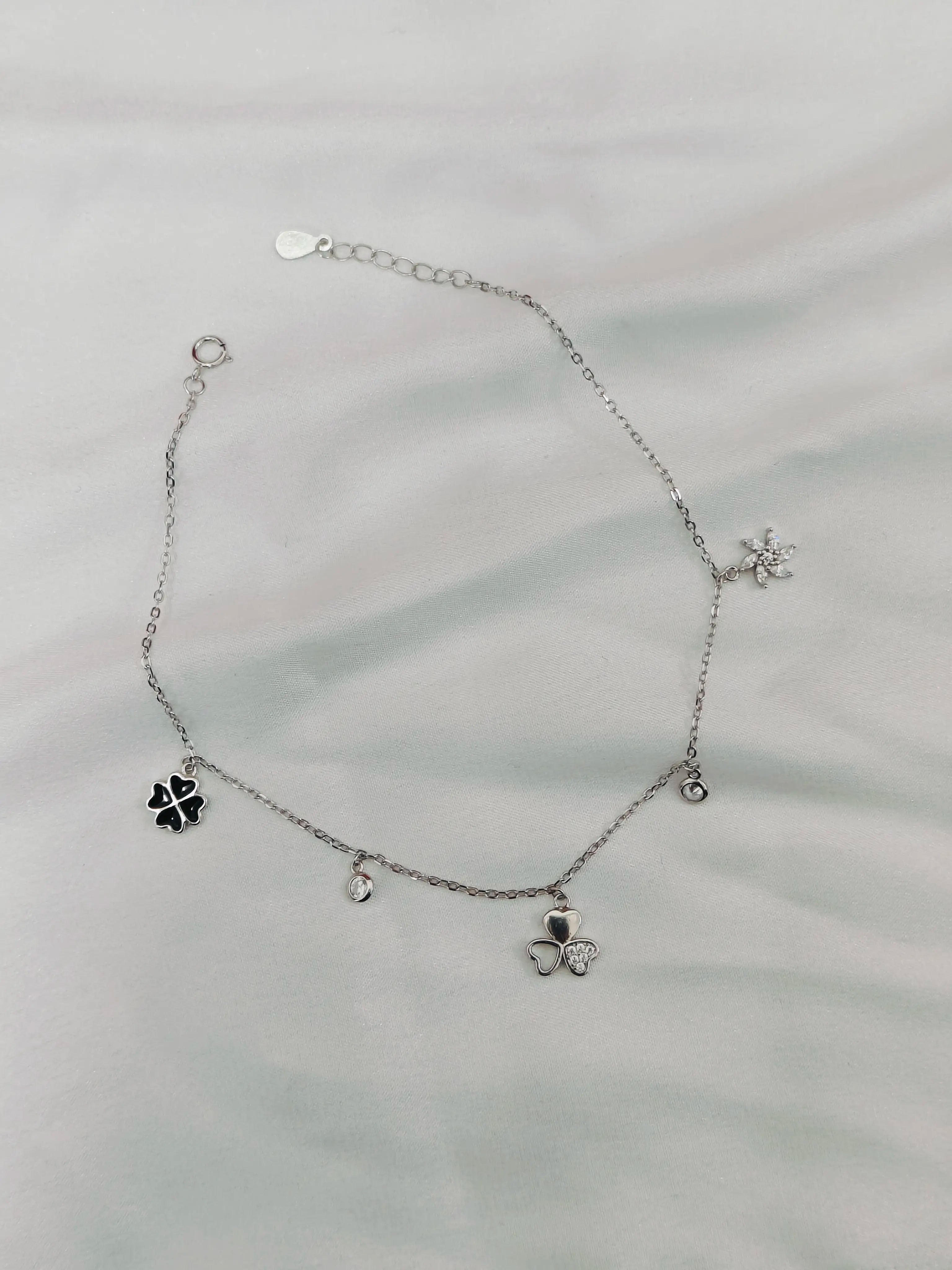 Silver anklet with clover-shaped charms on a light gray background